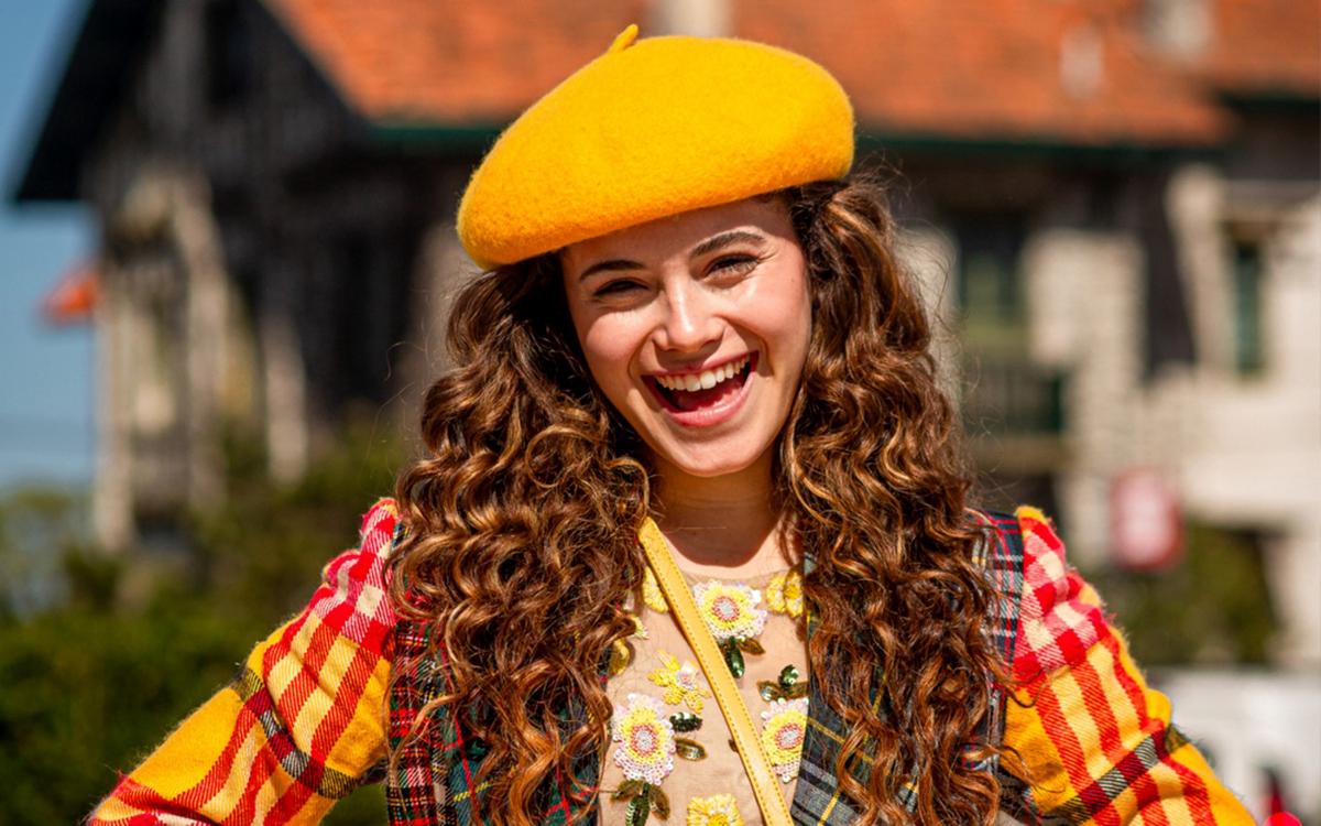 Joven con boina amarilla y ropa colorida sonriendo al aire libre, disfrutando de un día soleado.