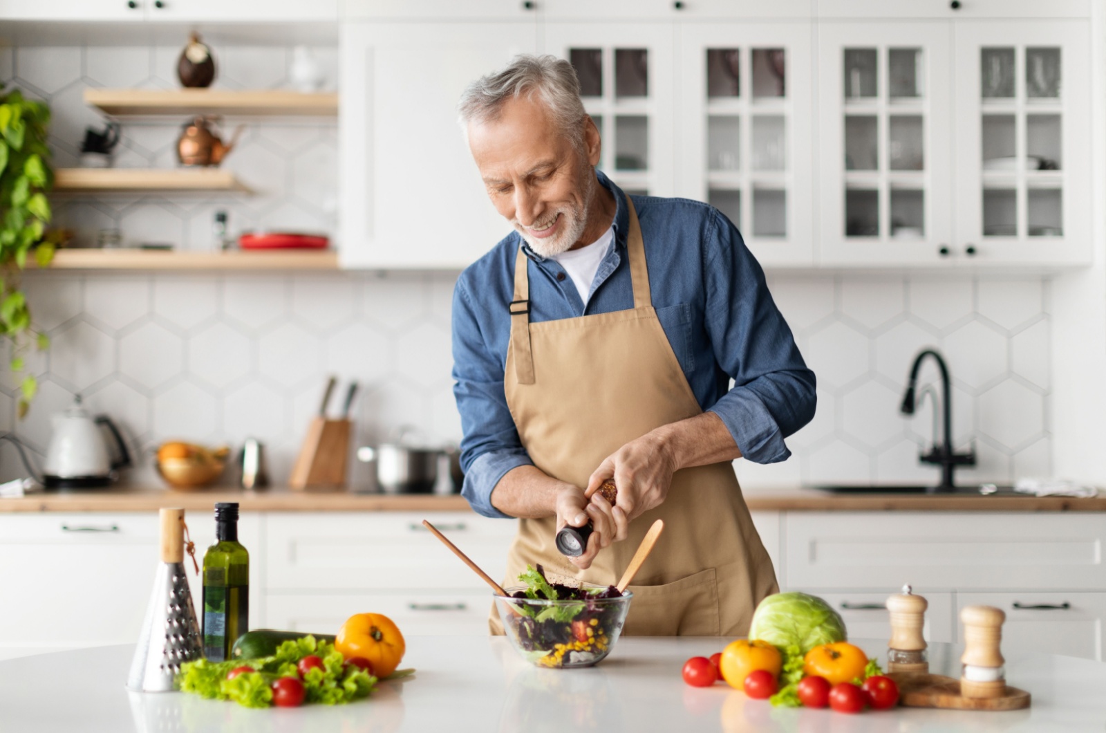 A smiling older adult grinding black pepper over a bowl of salad.