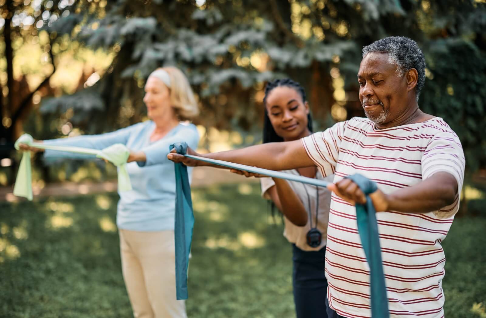 An instructor corrects a senior's form as they exercise with resistance bands in a sunny park.