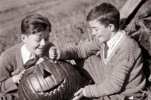 Two boys in the early 20th century carving pumpkins for Halloween.