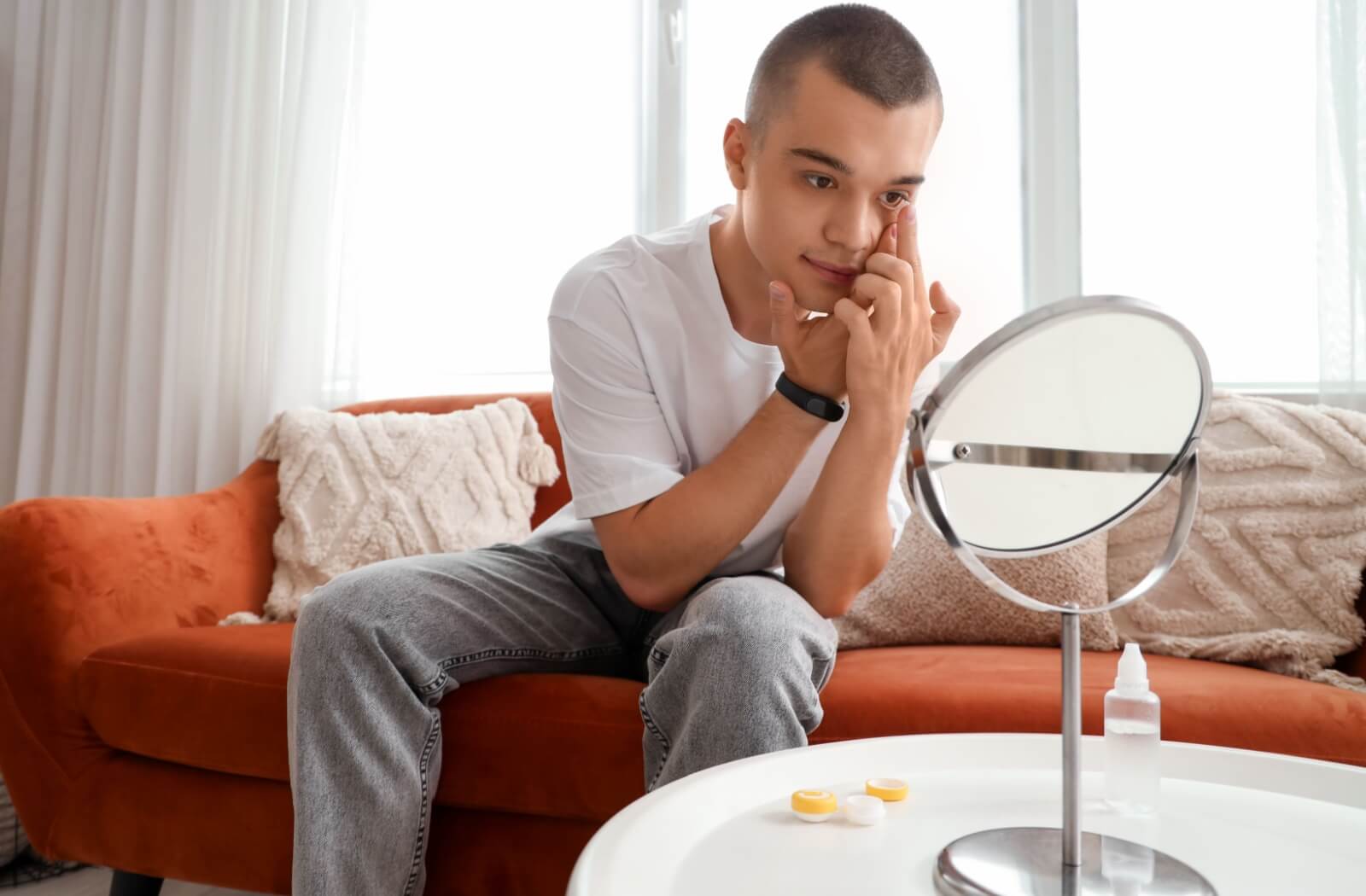 A young person putting in contact lenses while he looks into a mirror.