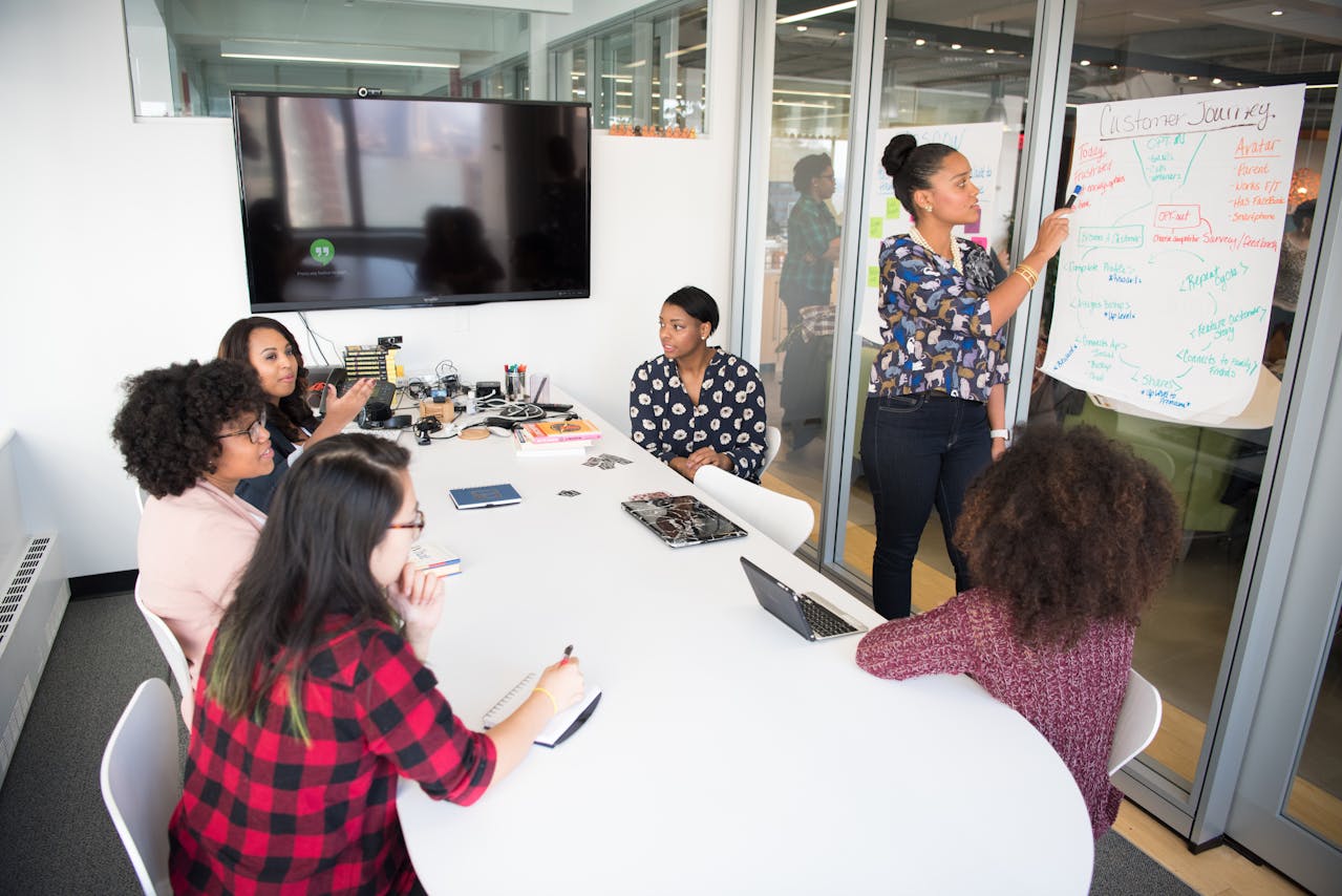 A group of professionals in a meeting room discussing strategies, with one person presenting on a whiteboard, demonstrating ways to improve team communication.