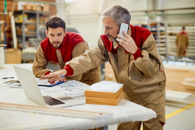 Carpenter talking on the phone while using computer in a workshop