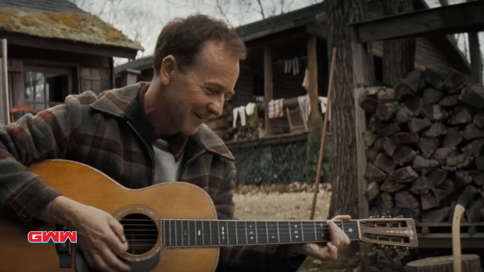 Pete Seeger plays an acoustic guitar outdoors, smiling contentedly.