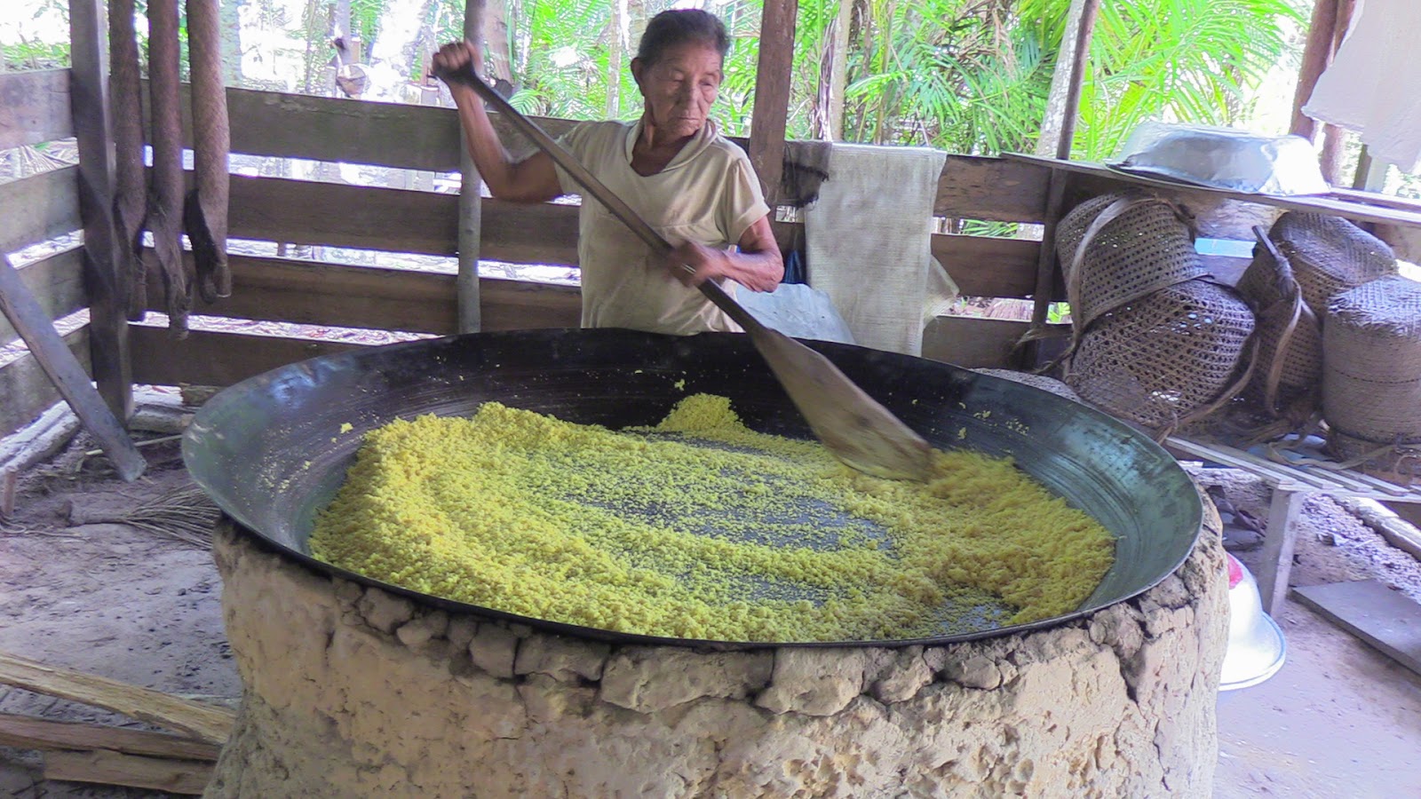 Dona Tereza torrando a farinha em um grande caldeirão. Ela usa uma pá grande para isso.
