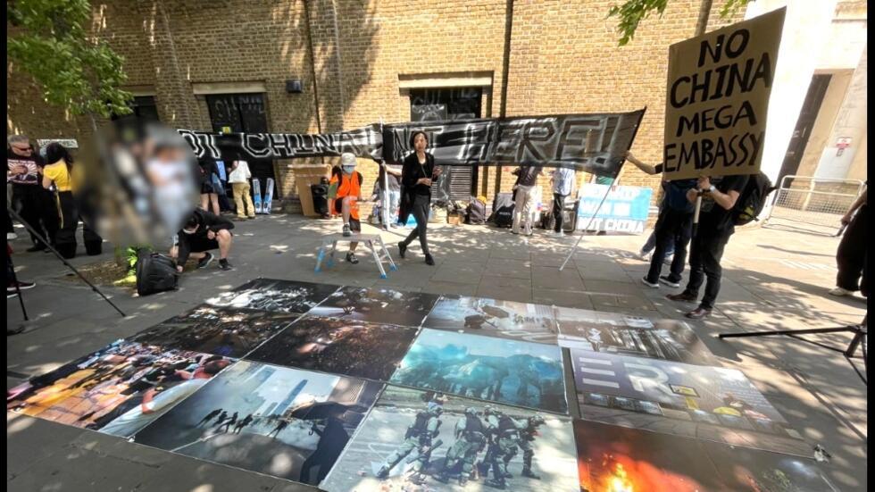 示威者反对兴建中国超级大使馆之馀，不忘展示中港政府2019年暴力打压示威的图片。2025年6月16日