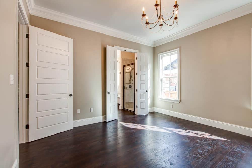 Primary bedroom with beige walls, dark hardwood flooring, and a private bath concealed in white double doors.