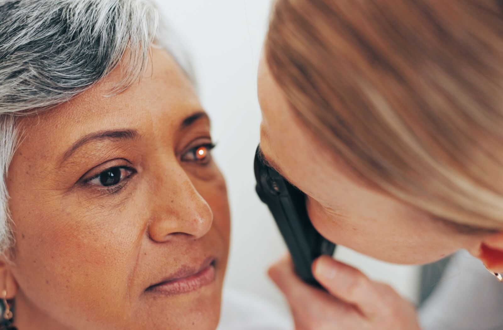 A person receives a close-up eye exam as a healthcare provider uses an ophthalmoscope to examine her retina.