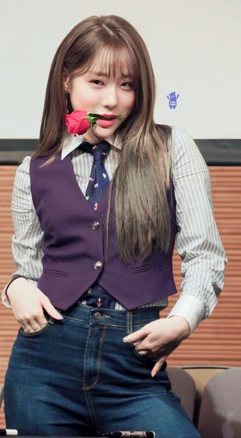 This contains an image of WJSN Yeonjung's with long hair wearing a purple vest and blue jeans, holding a pink flower in her mouth