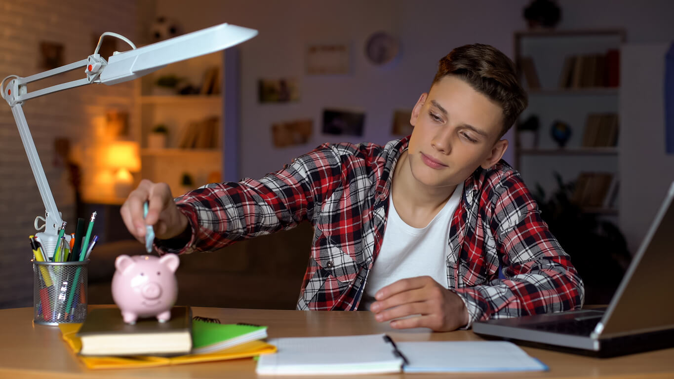 Un jeune homme fait ses comptes et met de l'argent dans sa tirelire. Il peut financer ses études et mettre de côté grâce à son job étudiant.