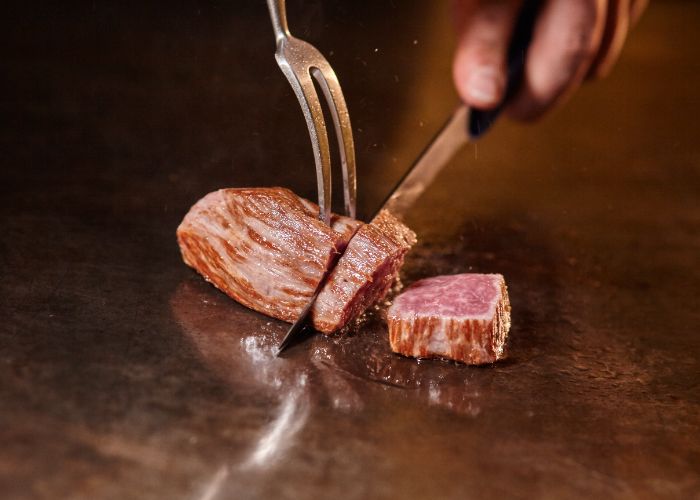 A small piece of Kobe beef being cut on the grill