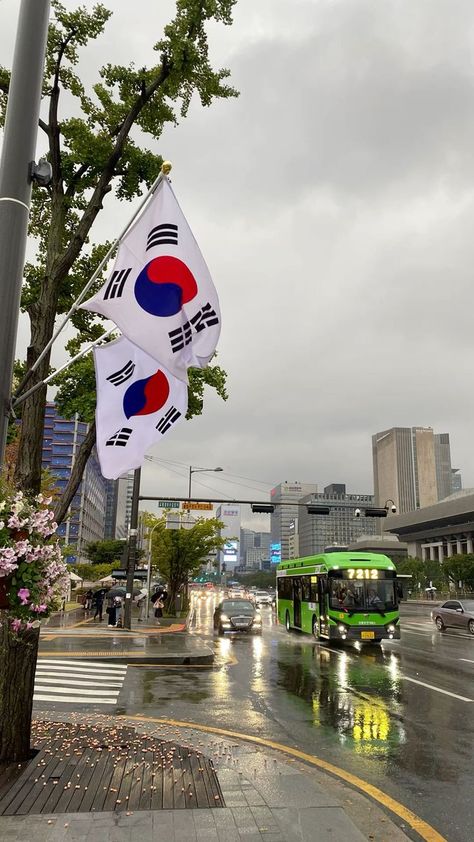 This contain an image of  two korean flags hanging from a pole on the side of a road in front of a green bus