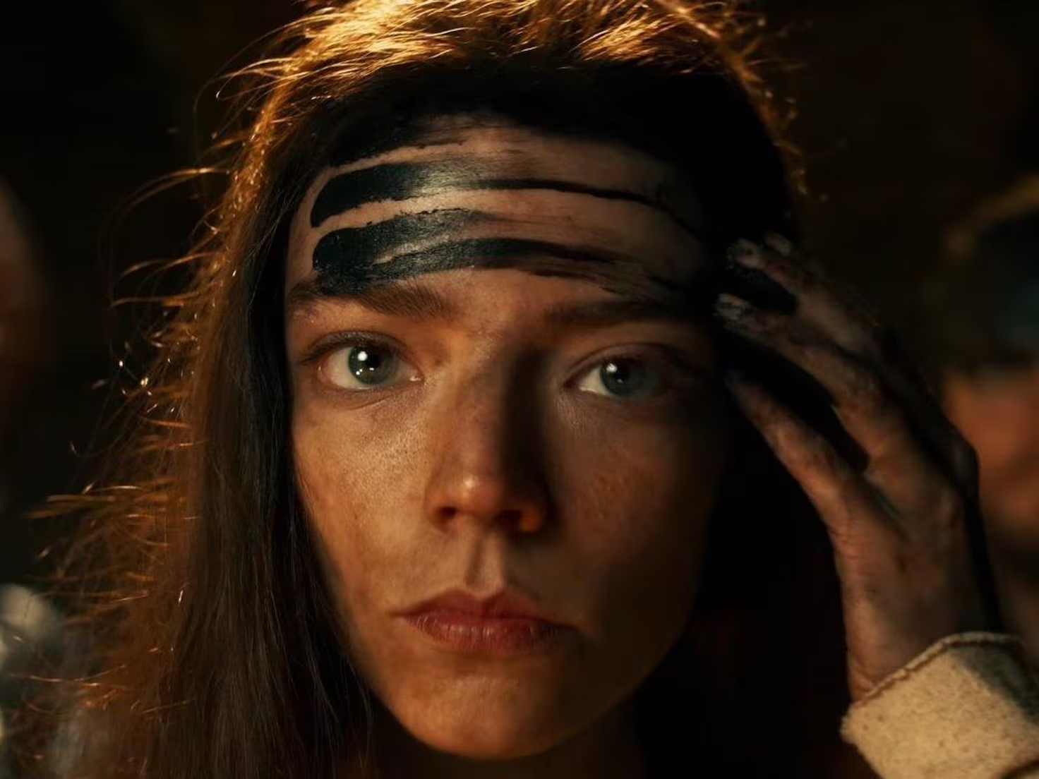 Anya Taylor-Joy con pintura negra en la frente en una escena intensa, mostrando un rostro decidido en un ambiente oscuro.