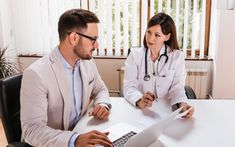 This  contain  two doctors sitting at a table looking at something on the computer screen and discussing to each other