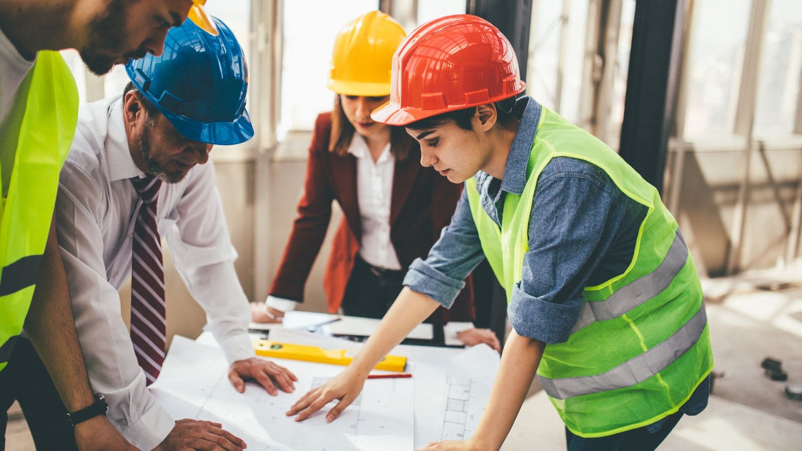 Group of people in hard hats and safety vests looking at blueprints.