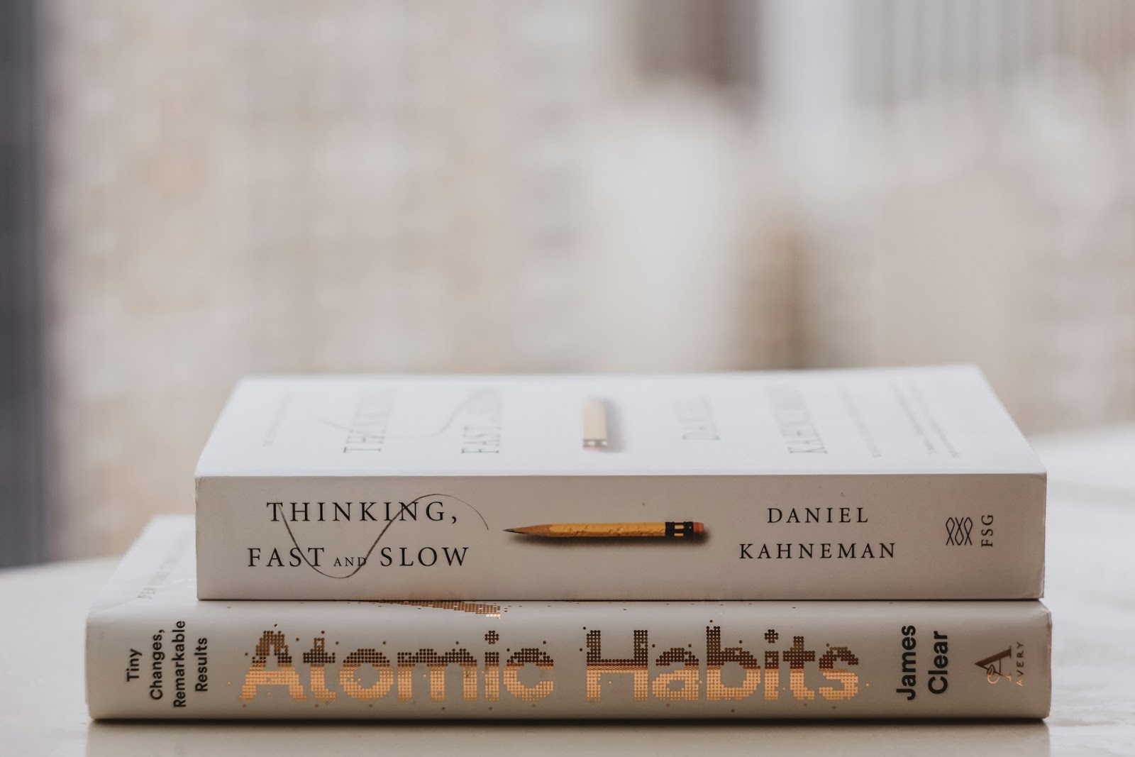 Two books resting on a table, with a title "Thinking Fast and Slow" and "Atomic Habits"