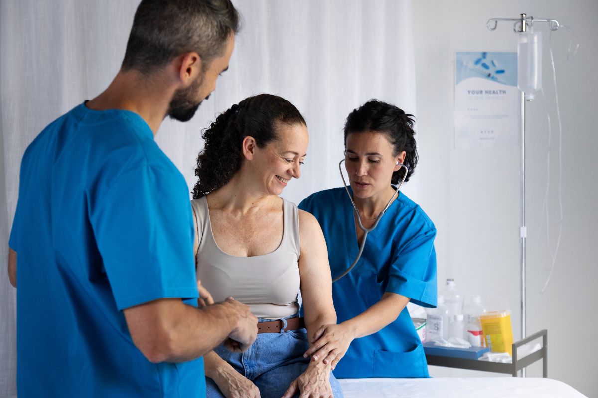 Paciente idosa recebendo atendimento de enfermagem no hospital, com sorriso e atenção dos profissionais de saúde durante o procedimento.