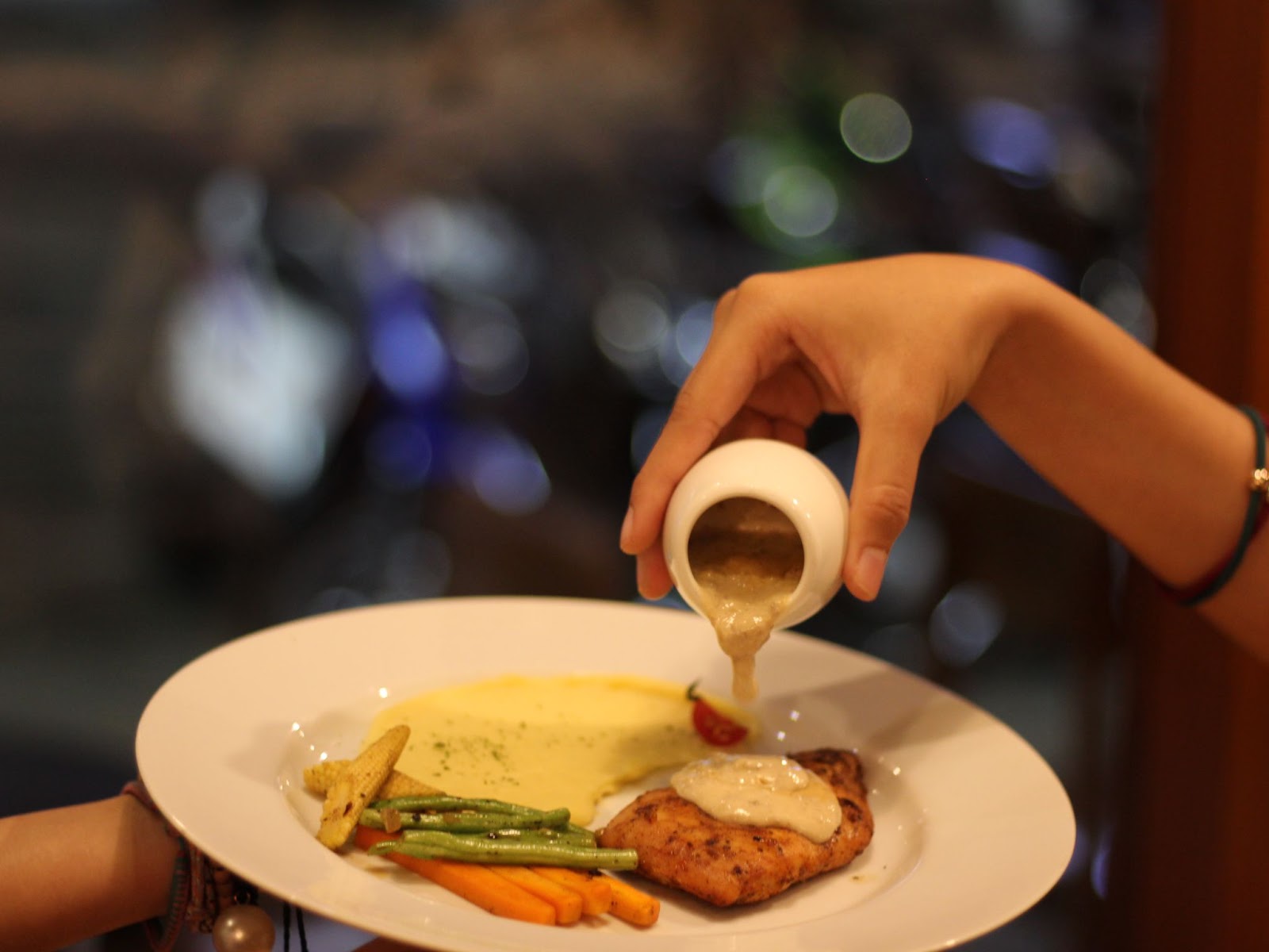 A cutlet served with vegetables on a plate, being drizzled with garlic sauce on top.
