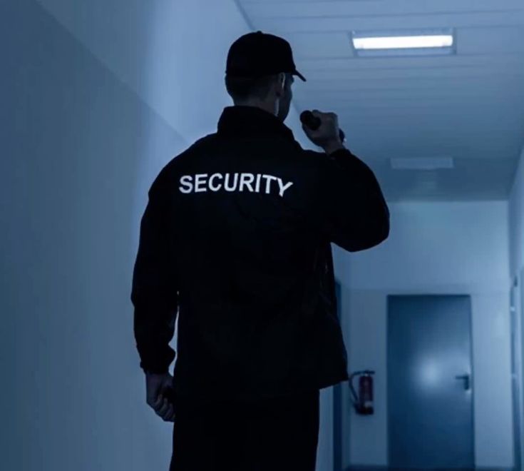 This contains an image of a security man walking down a hallway in an office building with the word security on his shirt