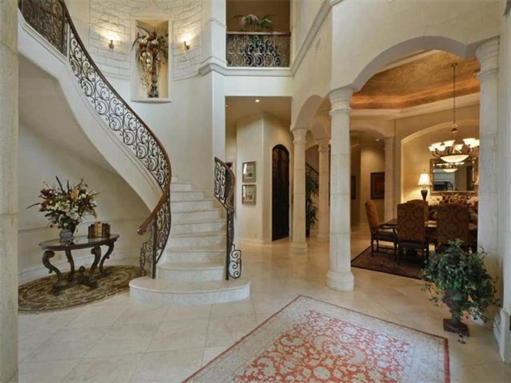 The foyer includes an intricate curved staircase complemented with a round center table.