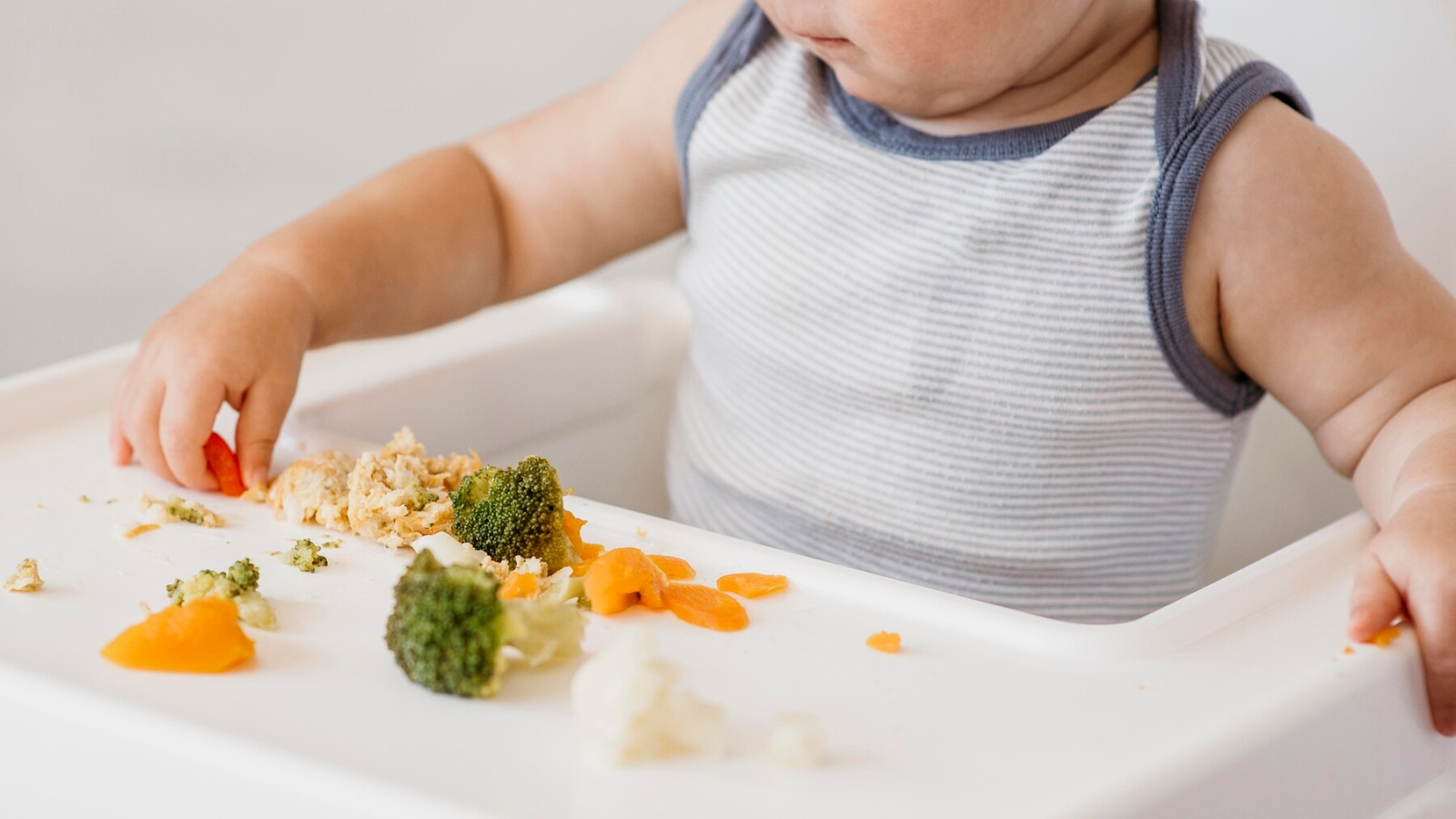 A baby boy in highchair choosing what to eat