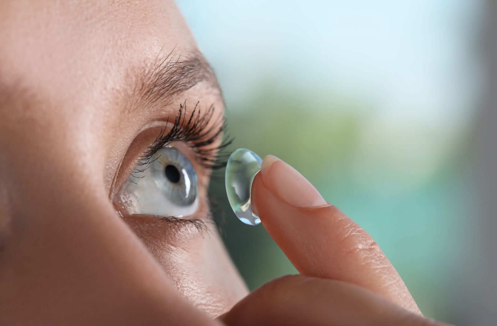 Close-up of a person about to insert a soft contact lens into their eye.