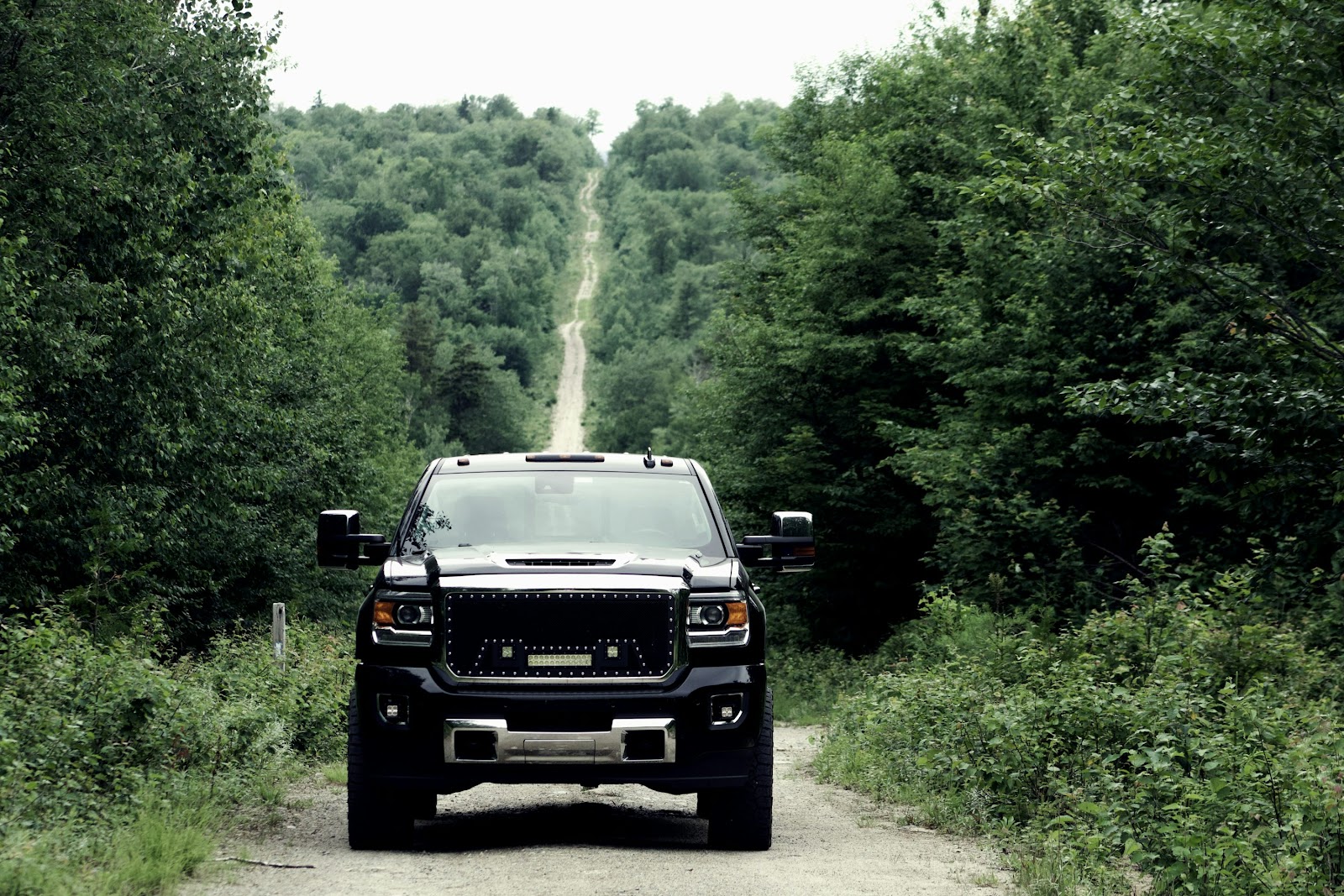 a truck driving down a dirt road through a forest