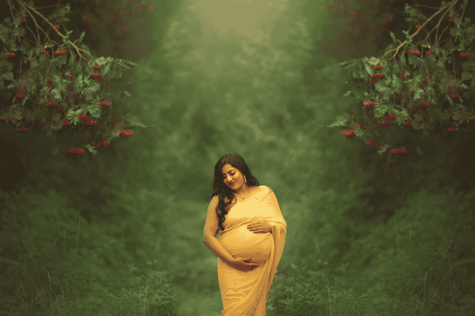 Pregnant woman in a vibrant yellow saree posing gracefully in a forest during a traditional maternity photoshoot