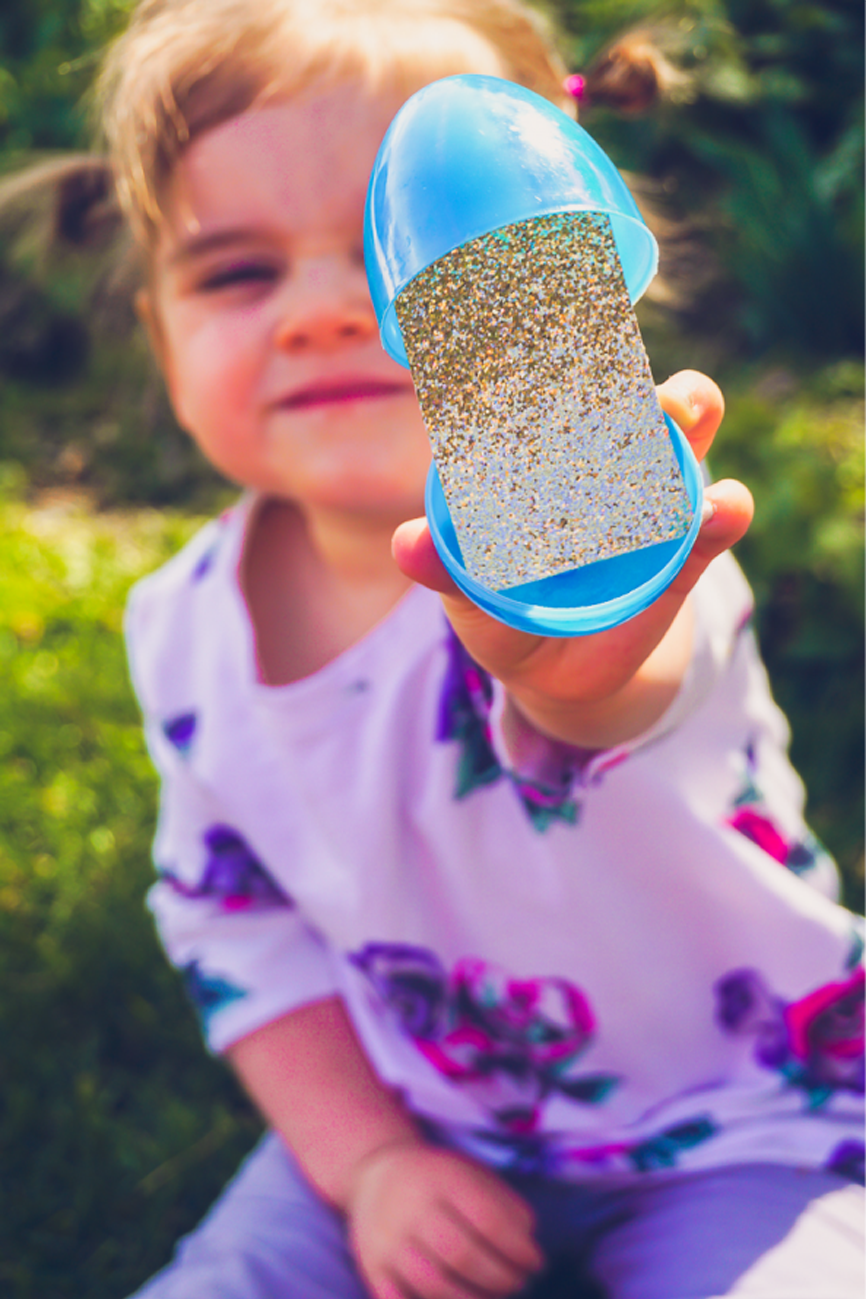 easter egg hunt ideas small girl holding a plastic blue egg opened to reveal glittery paper