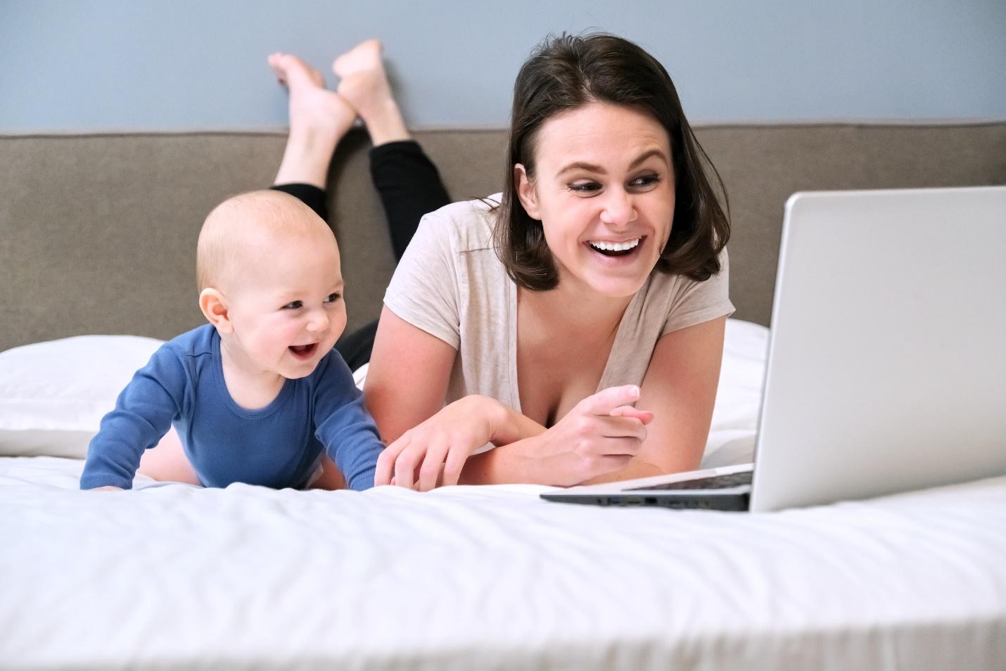 A person and baby lying on a bed looking at a computer

Description automatically generated