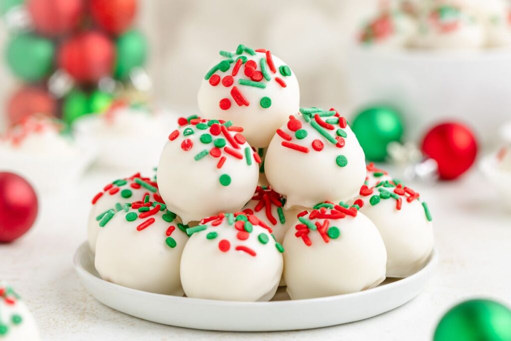 A white sugar cookie cock, topped with festive red and green sprinkles invested in the pyramid. The background shows decorations with blurred red and green jewelry.