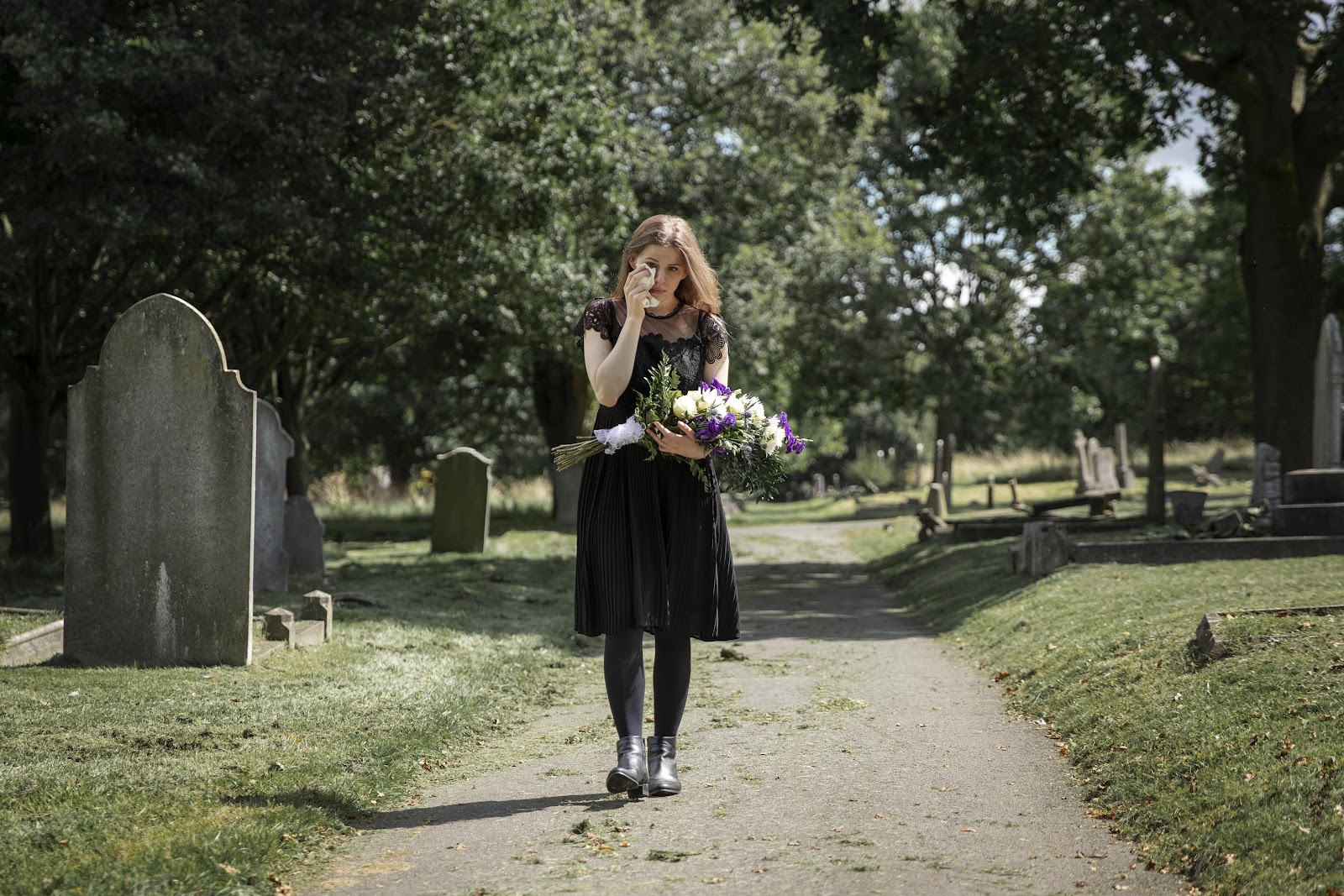 A grieving woman holding a bouquet of flowers in a cemetery | Source: Freepik