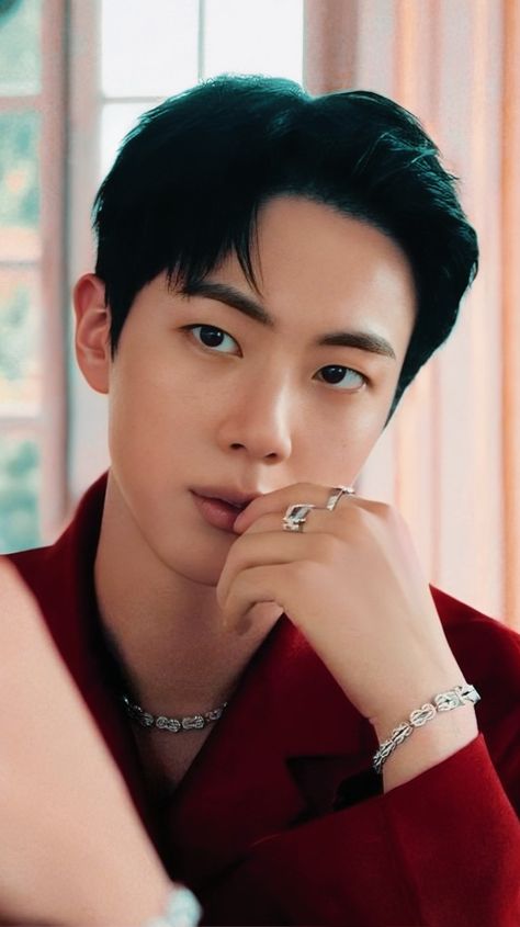 This contains an image of BTS Jin wearing a oxblood shirt with his hands on his lips