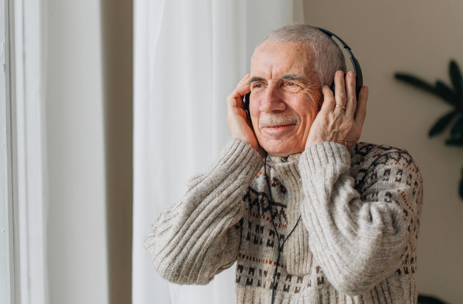 An older adult man listening to music using a pair of headphones.