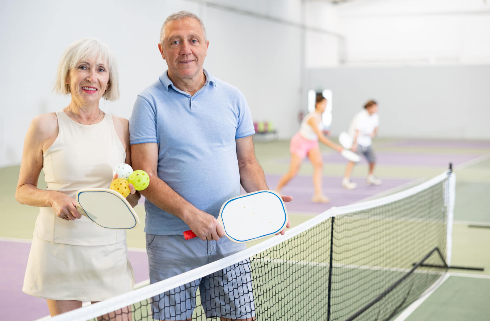 2 older adults on a pickleball court holding paddles and balls, getting ready to play a game and work on their cardio health.
