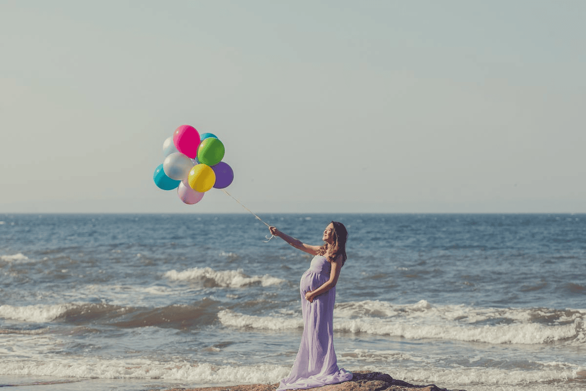 Pregnant woman enjoying a joyful moment with colorful balloons on the beach for maternity shoot