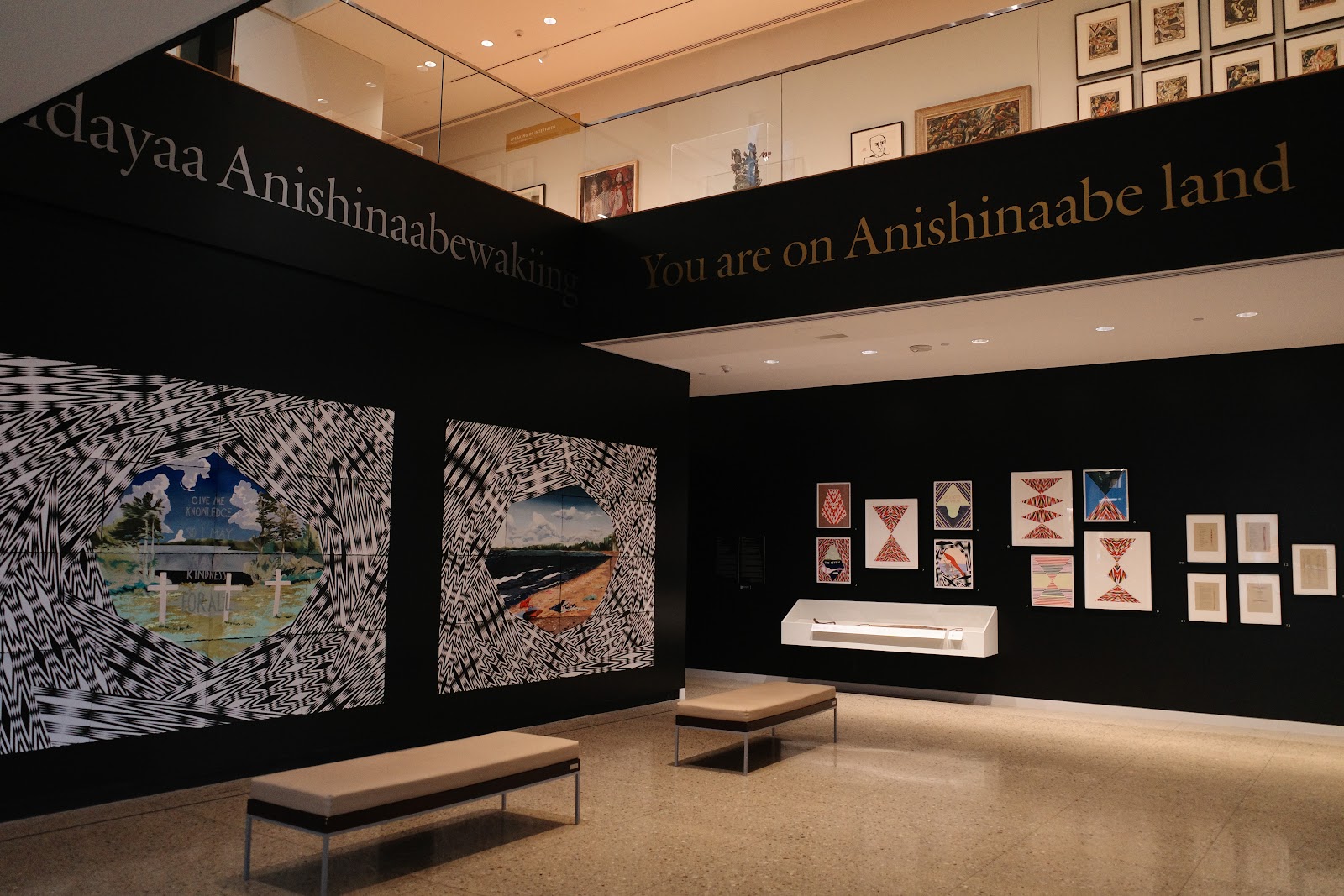 Art exhibition with paintings and drawings and wall text reading "You are on Anishinaabe land"