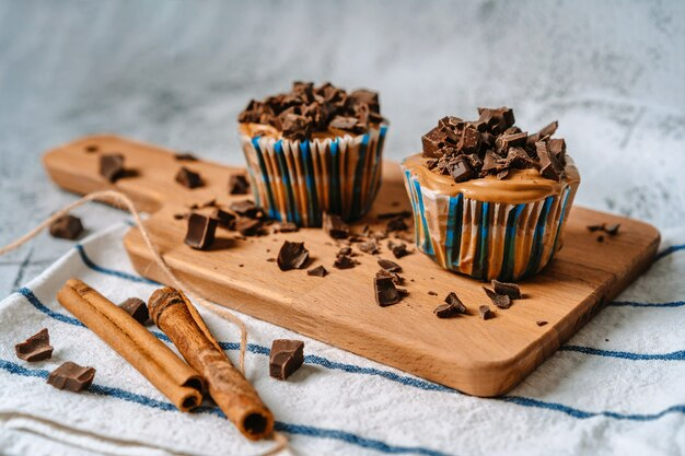 two cupcakes with chocolate and cinnamon on a wooden board