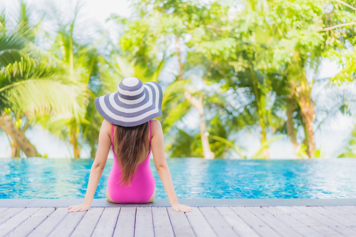 A girl sitting at the edge of a pool in a resort, enjoying the view.