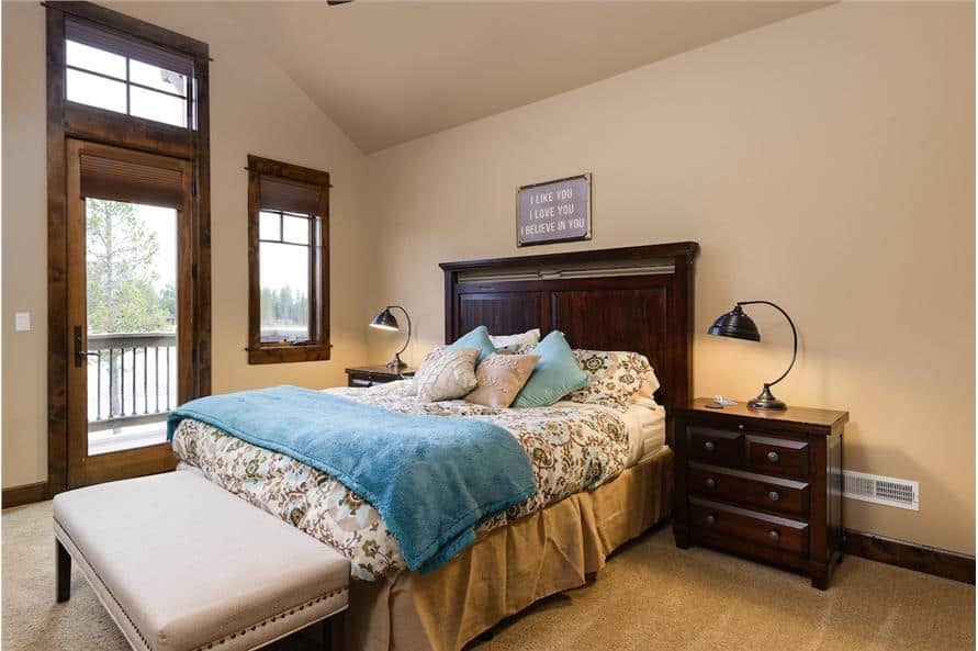 This bedroom has a vaulted ceiling, a skirted bed, a leather-upholstered bench, and a private deck accessible via a glass door.