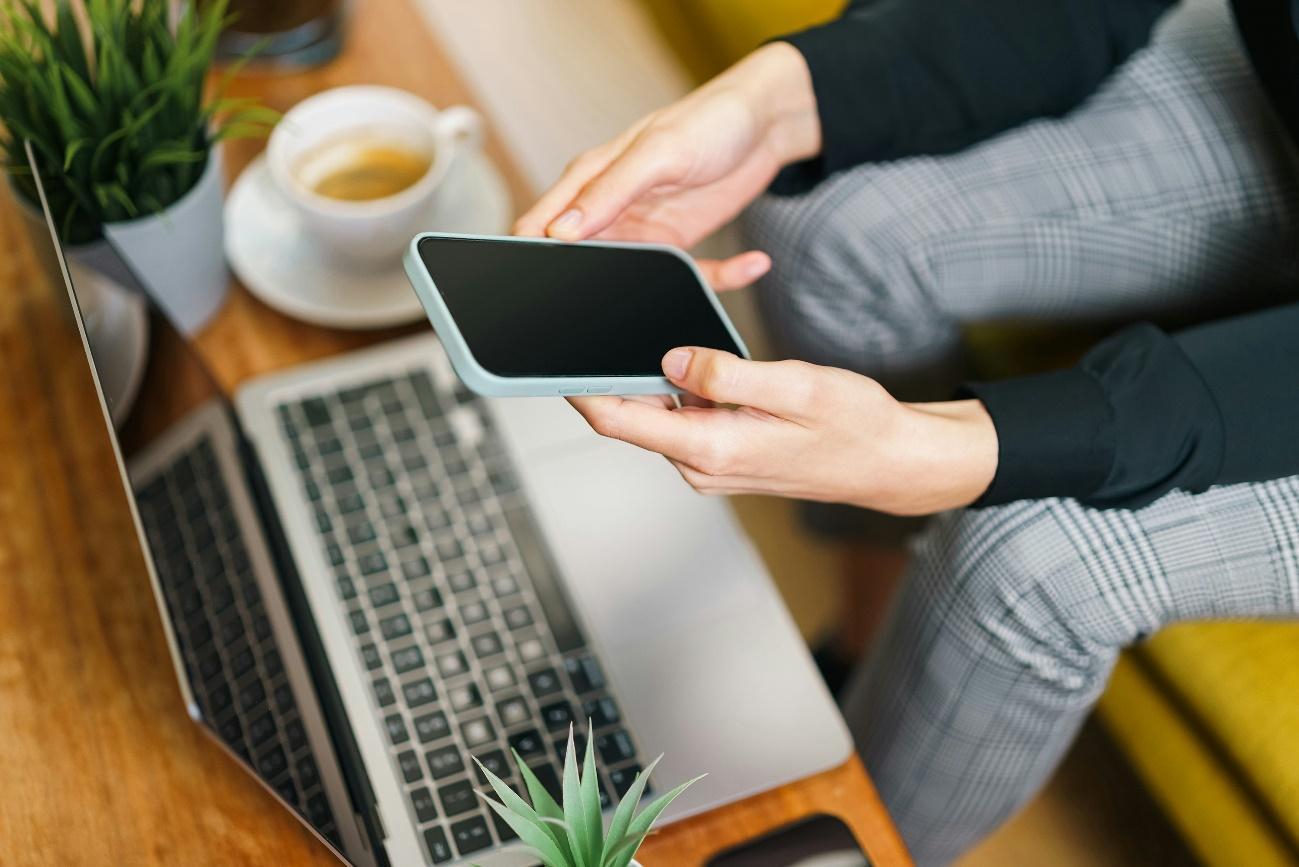 Una mujer sentada frente a una computadora portátil sosteniendo un teléfono celular