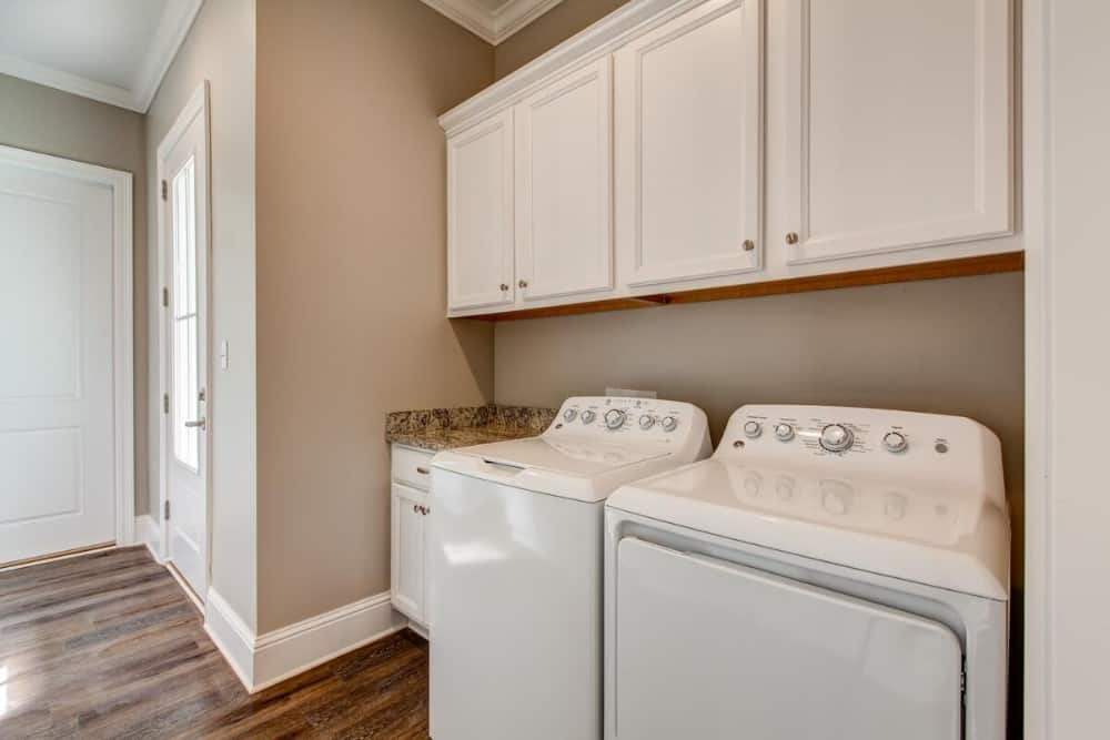 The laundry room is equipped with a top-load washer and dryer along with overhead cabinets.