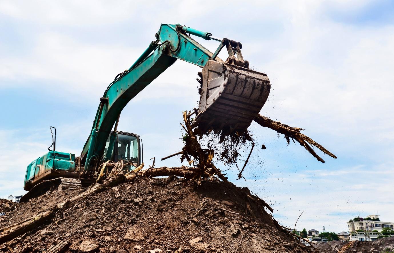 A green excavator digging a pile of dirt Description automatically generated