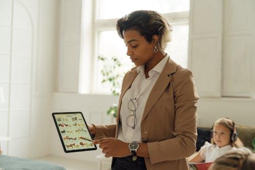 Free A teacher using a tablet in a bright classroom to explain a lesson to a student. Stock Photo