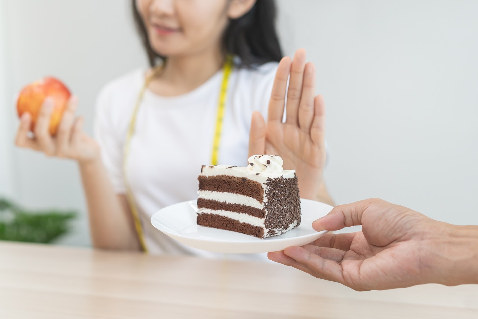 Femeie refuzând o felie de tort și preferând să mănânce un măr, pentru a-și reduce pofta de mâncare. 