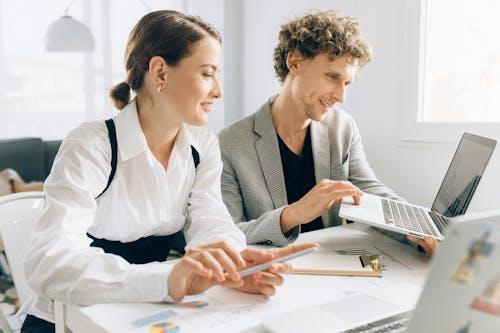 Free Two colleagues collaborating on a project, using laptops and documents in a modern office setting. Stock Photo