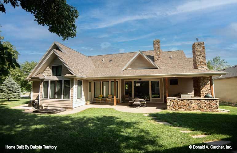 Rear exterior view showing the expansive porch filled with multiple seats, an outdoor dining set, and a summer kitchen with bar.