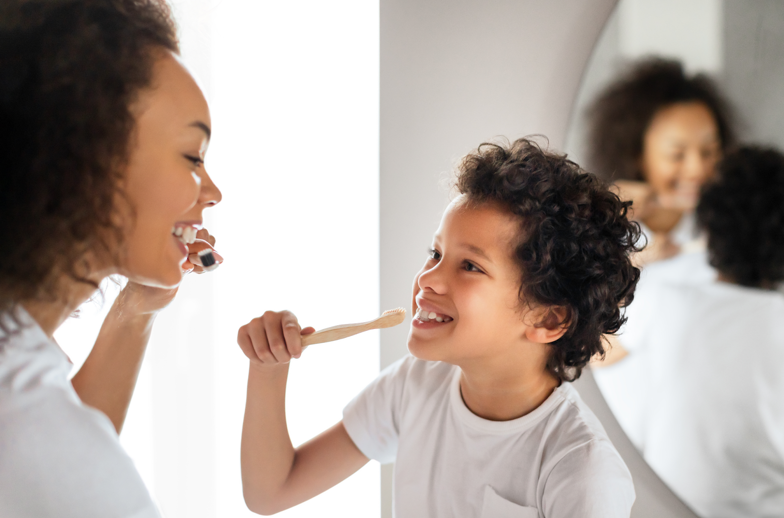  A parent and child brush their teeth together, smiling at each other.