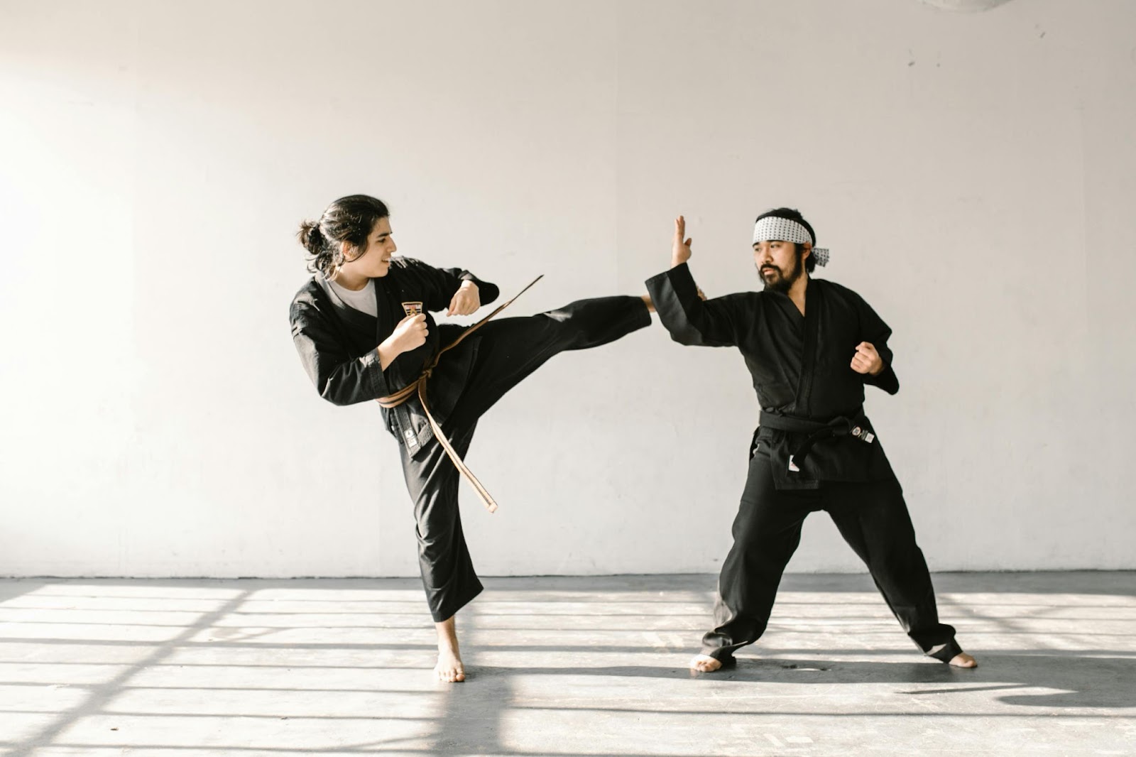 A martial arts instructor and a student practicing kicks together.