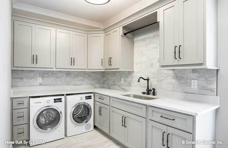 Laundry room with front-load washer and dryer, white cabinets, marble countertops, and a utility sink.